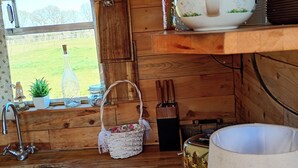 A rustic kitchen with wooden walls, a window with a view of a green field, a sink, a hanging basket, and a radio. - Beautiful Idilic Stay at The Box (Chichester)
