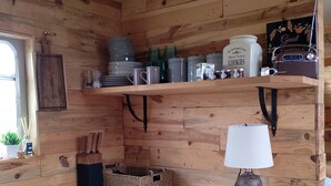 A compact kitchen with wooden walls, a small refrigerator, a sink, and a shelf with kitchenware and a radio. - Beautiful Idilic Stay at The Box (Chichester)