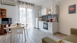 A modern kitchen with white cabinets, a dining area with a table and chairs, and a TV on a stand.