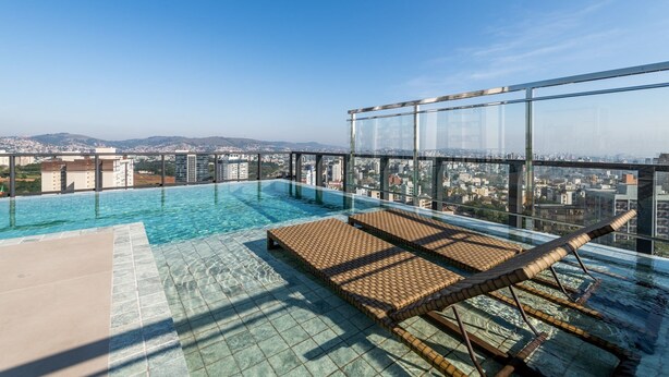 A rooftop infinity pool with a city view, glass walls, and lounge chairs. - LIV by LEMMON HOMES (Porto Alegre)