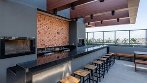 A rooftop bar with a brick wall, black countertops, and wooden stools. - LIV by LEMMON HOMES (Porto Alegre)