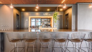 A modern bar area with a counter and metal chairs, featuring a sign that reads "LIV café". - LIV by LEMMON HOMES (Porto Alegre)