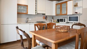 Een keuken met witte kastjes, een houten eettafel en een magnetron.