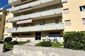 A multi-story building with balconies, a gated entrance, and a small garden area.