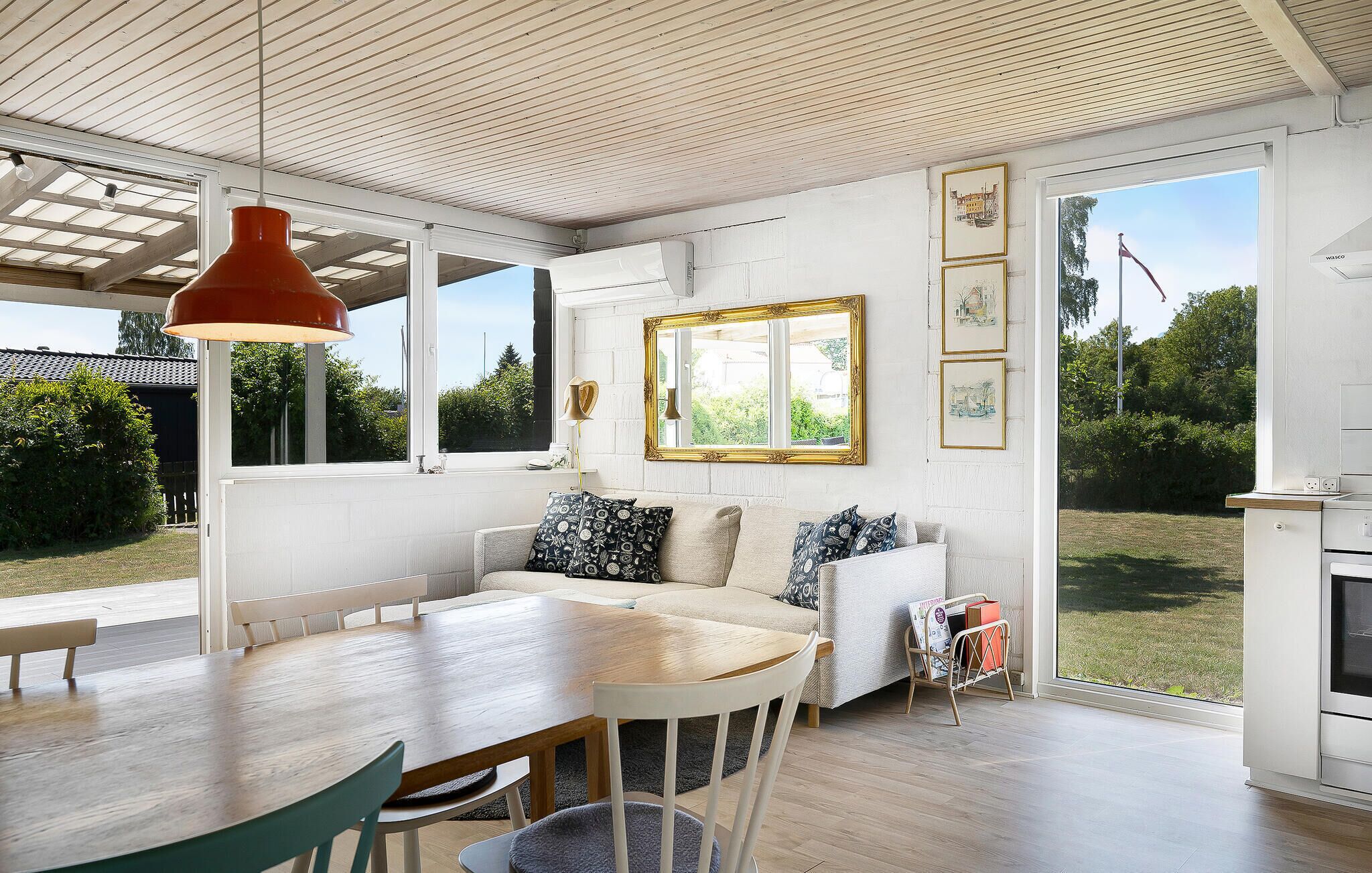 Una habitación amplia con una mesa de comedor de madera, un sofá con cojines estampados, un ventanal con vistas a la vegetación y un techo con vigas de madera.