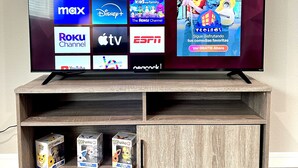 A flat-screen TV on a wooden TV stand with a shelf below displaying Funko Pop! figurines.