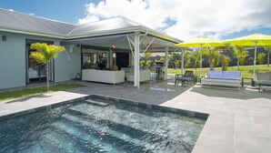 Una casa moderna con piscina, mobiliario de exterior y un patio cubierto.