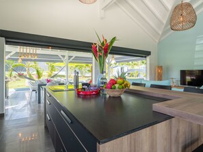A modern kitchen with a large island, a dining area with a TV, and a view of the outdoors. - Villa Maxence remarkable elegance, experience a dream getaway (Saint-François)