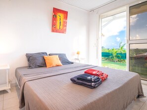 A bedroom with a bed, pillows, a blanket, and a towel. There is a window with a view of greenery. - Villa Ti'Punch with a sea view from the infinity pool (Sainte-Anne)