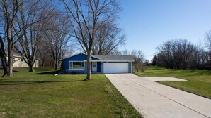 Une petite maison de plain-pied avec un garage, entourée d’arbres et d’une pelouse.