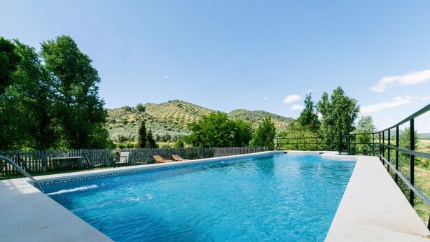 Piscina rectangular con agua azul cristalina, rodeada por una valla de madera, y vista a un paisaje montañoso al fondo.