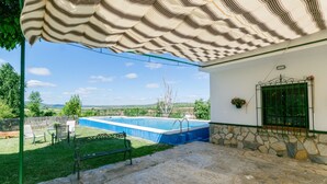 Piscina con pared de piedra y reja de metal, una banca y vista al campo.