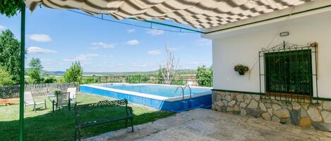 A swimming pool with a stone wall and a metal gate, a bench, and a view of the countryside.