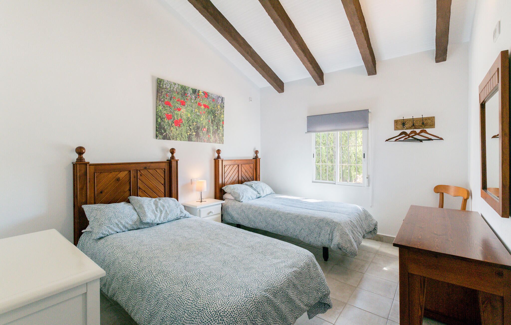 Une chambre avec deux lits, une tête de lit en bois, une table de chevet avec une lampe, une fenêtre donnant sur un beau paysage et un tableau accroché au mur.