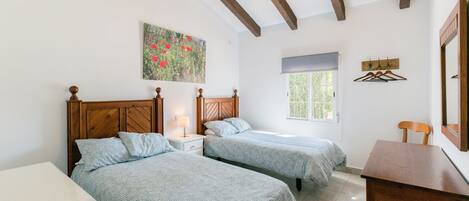 Une chambre avec deux lits, une tête de lit en bois, une table de chevet avec une lampe, une fenêtre donnant sur un beau paysage et un tableau accroché au mur.