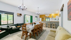 Comedor con mesa lista para seis personas, rodeada de sillas de madera. Hay un sofá y un sillón en la sala.