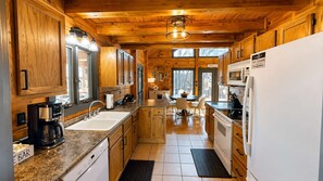 A kitchen with wooden cabinets, a coffee maker, a sink, a dining area with chairs, and a refrigerator. - Ridge Hideaway • Peaceful Lake Escape (Cadiz)
