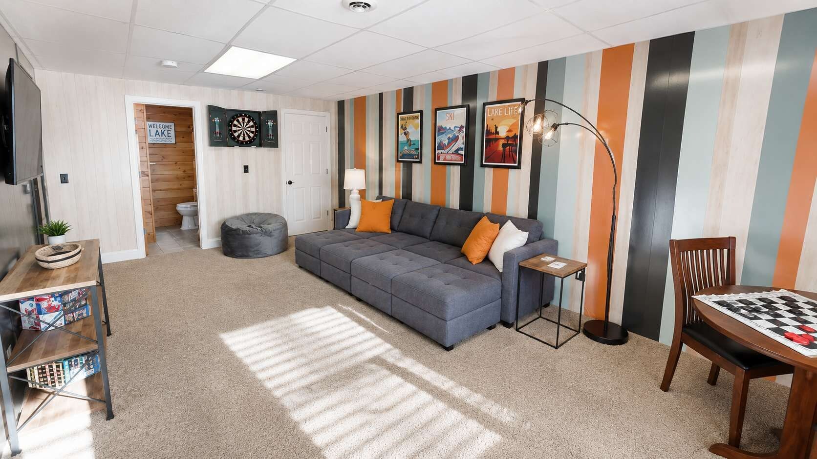A living room with a grey sofa, a coffee table, a dartboard, and striped wallpaper.
