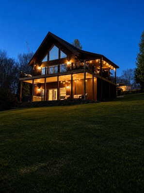 A two-story wooden house with a balcony, a covered porch, and a well-lit interior. - Ridge Hideaway • Peaceful Lake Escape (Cadiz)