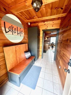 Un intérieur en bois avec un banc, une porte et une pancarte sur laquelle on peut lire « Vie au bord du lac ».