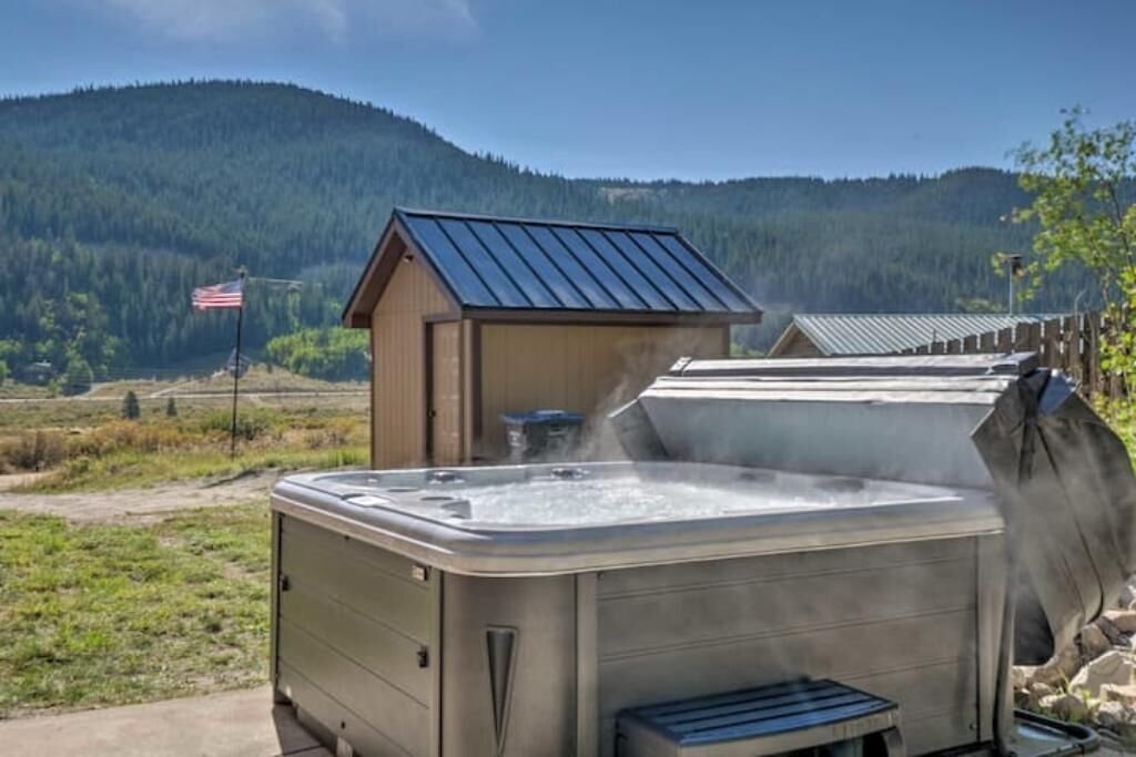 Een hottub met een metalen dak, omgeven door een houten terras en een kleine schuur met een Amerikaanse vlag.
