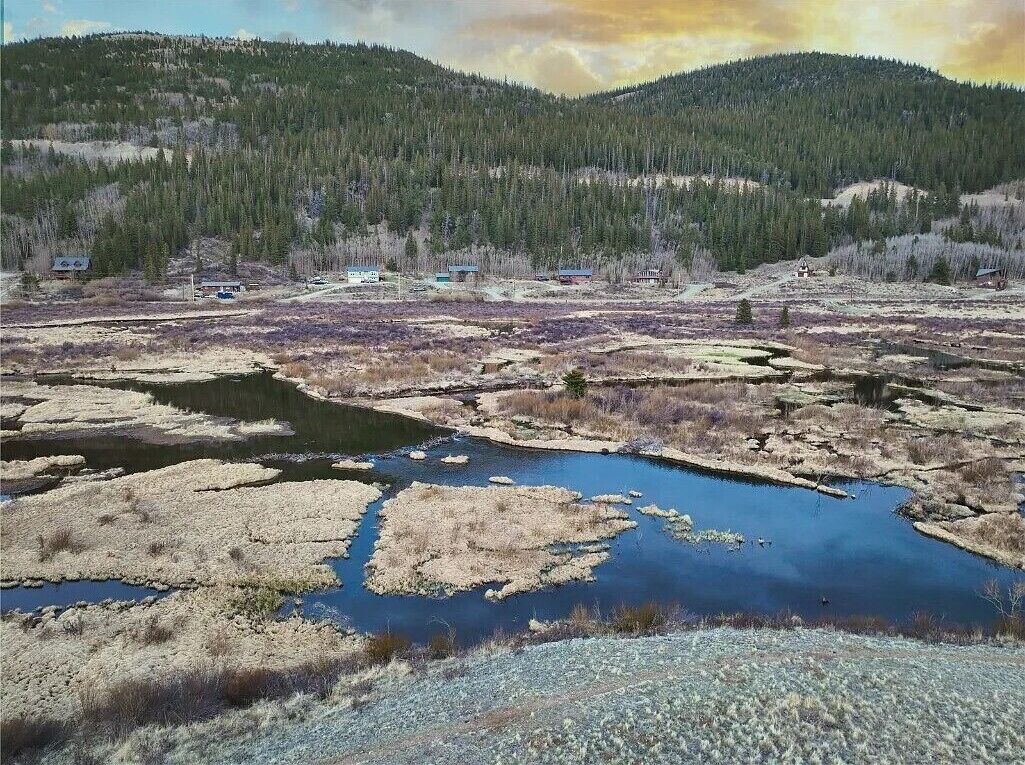 Paisaje natural con río, colinas boscosas y pequeñas construcciones.