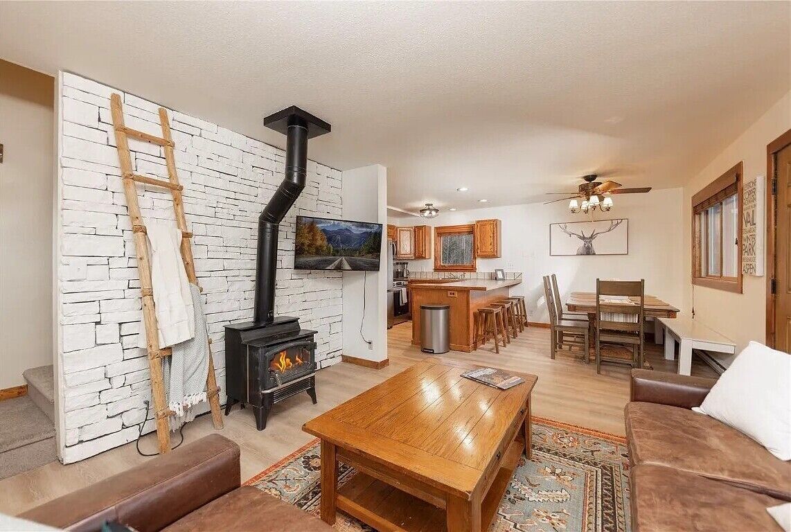 Un salon chaleureux avec une cheminée, des meubles en bois et un coin cuisine à l’arrière-plan.