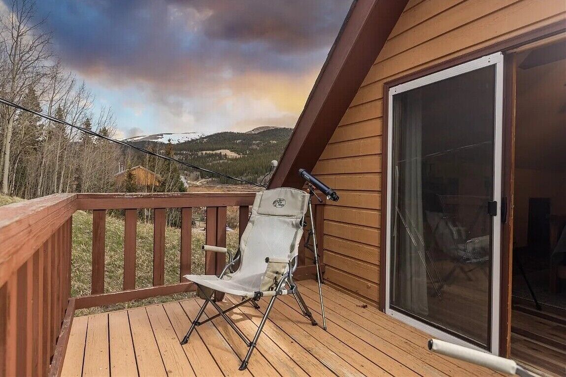 Una terraza de madera con una silla plegable y un telescopio, con vistas a un paisaje nevado.
