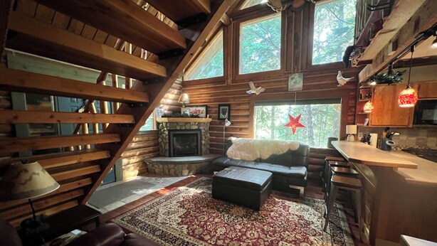 A cozy cabin interior with a stone fireplace, wooden beams, a leather sofa, and a large rug.