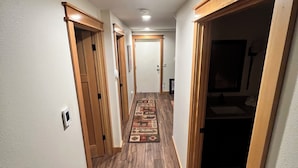 A narrow hallway with wooden flooring and doors on both sides.
