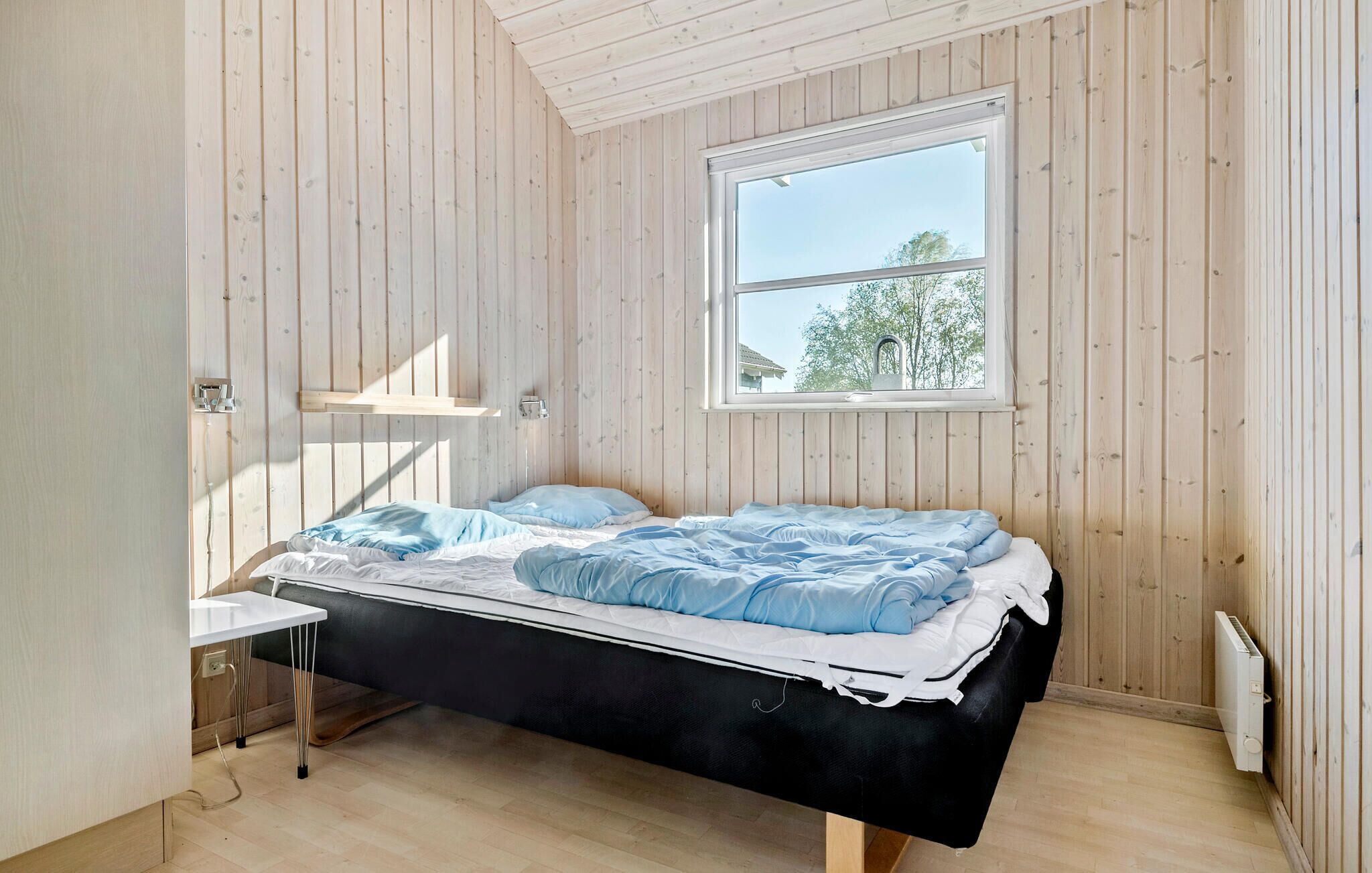 Ein Schlafzimmer mit einem Bett, einem Fenster, einer Heizung und einer Holzwand.