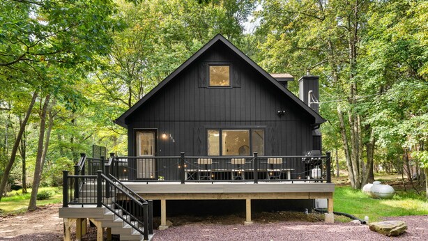 A dark wooden cabin with a deck, surrounded by trees.