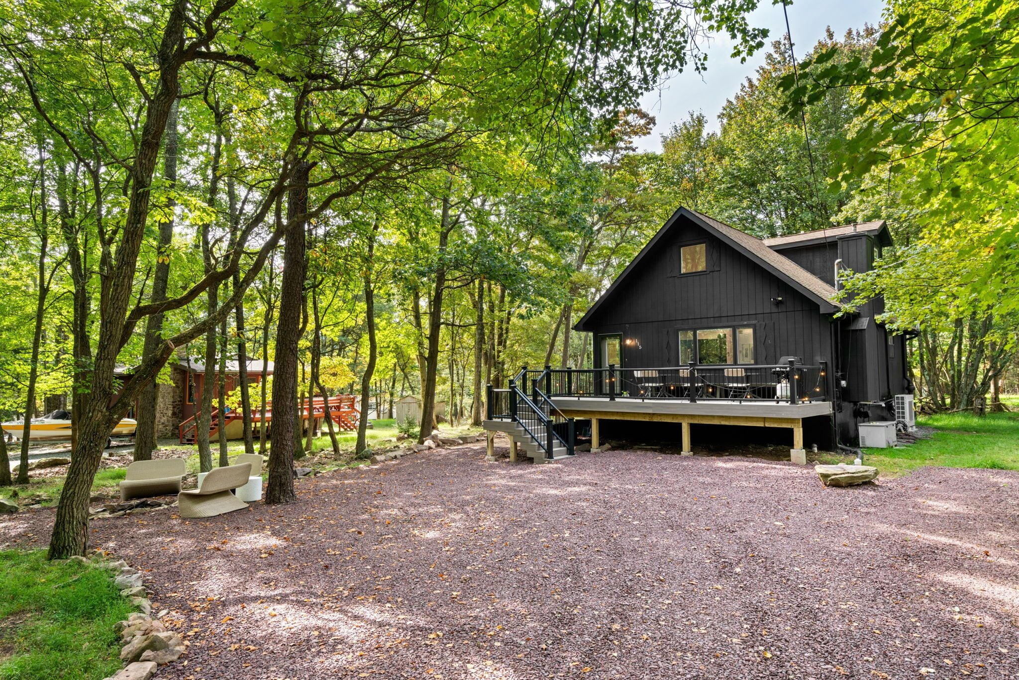 Une cabane dotée d’une terrasse, entourée d’arbres et de gravier.