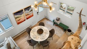 A dining area with a round table, chairs, and a chandelier. There are paintings on the walls and a large horn sculpture.