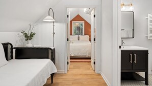 A bedroom with a bed, bedside table, lamp, and a view into an adjacent room with a window.