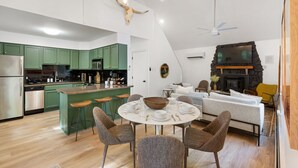 A modern kitchen with green cabinets, a dining area with a round table, and a living room with a sofa and a fireplace.