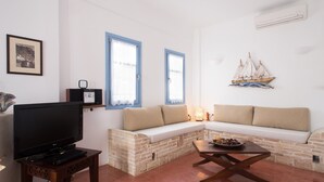 A living room with a TV, a stone bench, a wooden coffee table, and a wall-mounted ship decoration. - Daphne | Cycladic Three-Bedroom Villa with Private Pool and Sea View (Thira - Santorini)