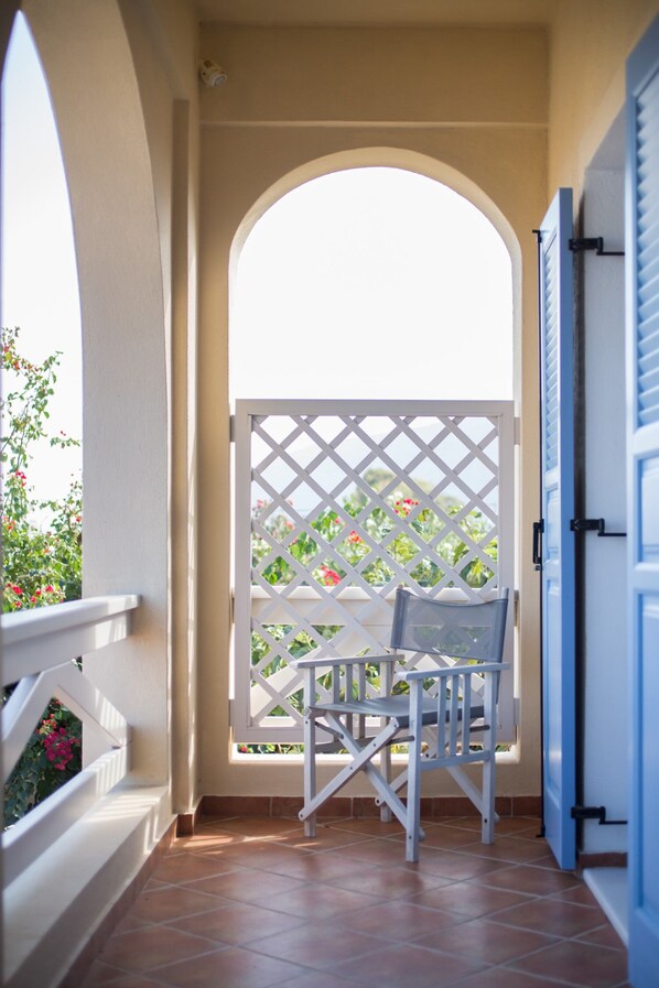 A balcony with a white lattice partition, a chair, and a view of greenery. - Daphne | Cycladic Three-Bedroom Villa with Private Pool and Sea View (Thira - Santorini)