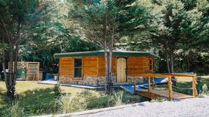Une cabane en bois avec des fondations en pierre, une terrasse en bois et un petit porche.