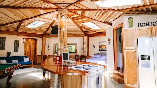 L’intérieur d’un chalet rustique, avec un plafond en bois, un coin repas, une cuisine équipée d’une cuisinière, un lit et un réfrigérateur.