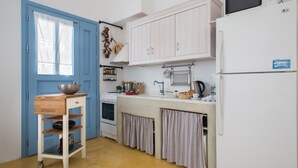 Uma cozinha compacta com porta azul, armários brancos, geladeira branca, micro-ondas, pia e prateleira de madeira com uma tigela.