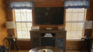 Ein gemütliches Wohnzimmer mit einem großen Fernseher, Holzwänden und einem runden Couchtisch.