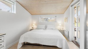 Un dormitorio con techo de madera, un ventanal grande, dos lámparas de noche y una cama con ropa blanca.