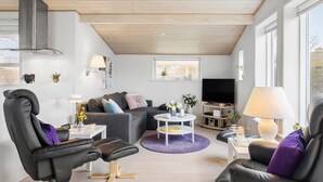 Una sala de estar moderna con un sofá gris, sillas de cuero negro, una mesa de centro blanca y un televisor.