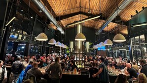 A crowded indoor dining area with exposed ductwork, pendant lighting, and large windows. - 1960s Gem-Close to Downtown & In a Quiet Area (Cedar Rapids)