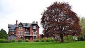 A large, two-story brick house with a well-maintained lawn and a large tree in front. - 1960s Gem-Close to Downtown & In a Quiet Area (Cedar Rapids)