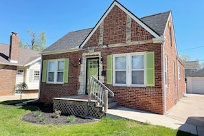 A two-story brick house with a front porch, green shutters, and a garage.