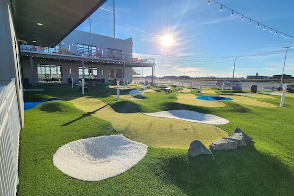 A modern building with a covered outdoor area, artificial grass, and a sunlit sky.