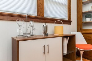 A kitchenette with a wooden countertop, a white cabinet, and a white chair with an orange cushion.