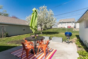 Eine Terrasse mit einem runden Tisch, orangefarbenen Stühlen, einem grünen Sonnenschirm und einem Grill.